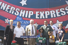 [Photo 3: New homeowners and dignitaries standing in front of the Homeownership Express Bus]