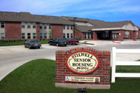 [Photo 1: The entrance sign 'Stilwell Senior Housing - Loving One Another' with the 40-unit complex in the background]