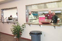 [Photo 2: John in the middle of two men cooking]