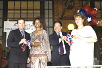 [Photo 1: Two new homeowners holding ribbons and two representatives]