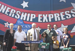 [Photo 4: New homeowners and dignitaries standing in front of the Homeownership Express Bus]