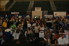 [Photo: Wide-angle view from the stage of the gymnasium filled with people, booths, balloons, and activity]
