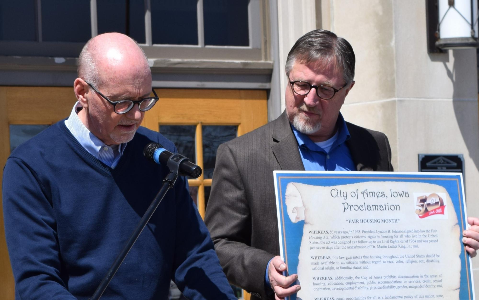 Mayor Haila reads the Proclamation while Field Office Director Eggleston holds a life size version of the proclamation
