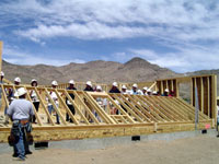 [Photo 1: 17 people raising frame of new home's wall together]