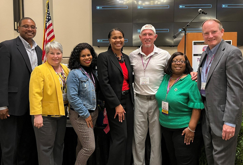 [Dr. Felicia Gaither, PIH Deputy Assistant Secretary for Field Operations (center) is welcomed by Region IV teammates following her Opening Session keynote remarks at the Kentucky Housing Association/Tennessee Association of Housing and Redevelopment Authorities Annual Training Conference.  Pictures are Will Biggs, Tennessee PIH Director; Carol Spencer, Kentucky PIH Director, Tajuanya Carr, Nashville Field Office Portfolio Management Specialist; J. Shannon Cross, Knoxville Field Office Portfolio Management Specialist; Cynthia Mitchell, Tennessee PIH Division Director; and Walter Perry, Nashville Field Office Director.]