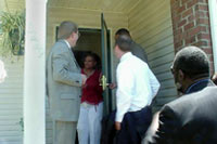 [Photo 3: Woman at front door of her new home welcomes tour]